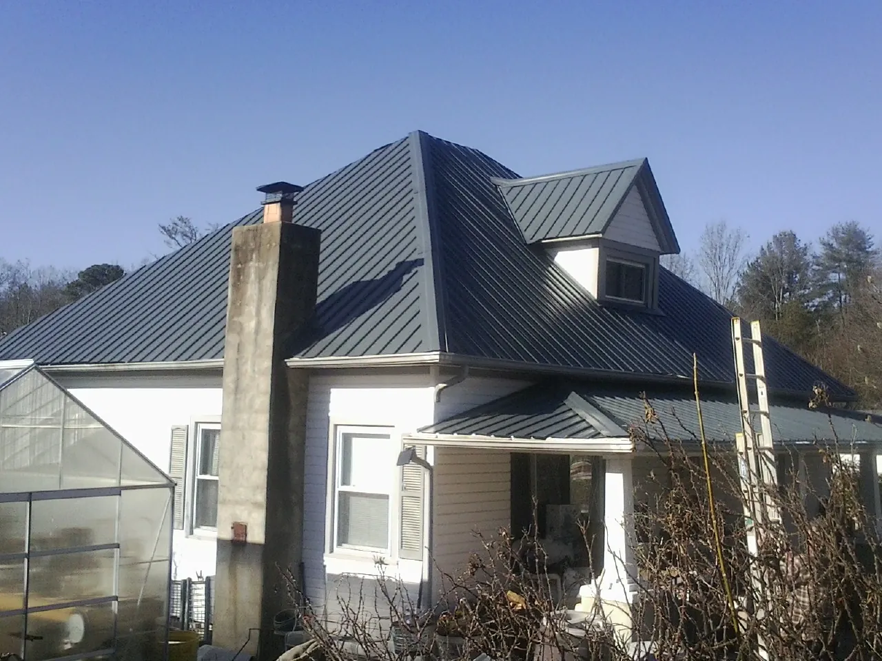 Dark blue standing seam metal roof on a white farmhouse with dormer — Slate & Tile Roof Repair by Roofing Brothers in Bismarck