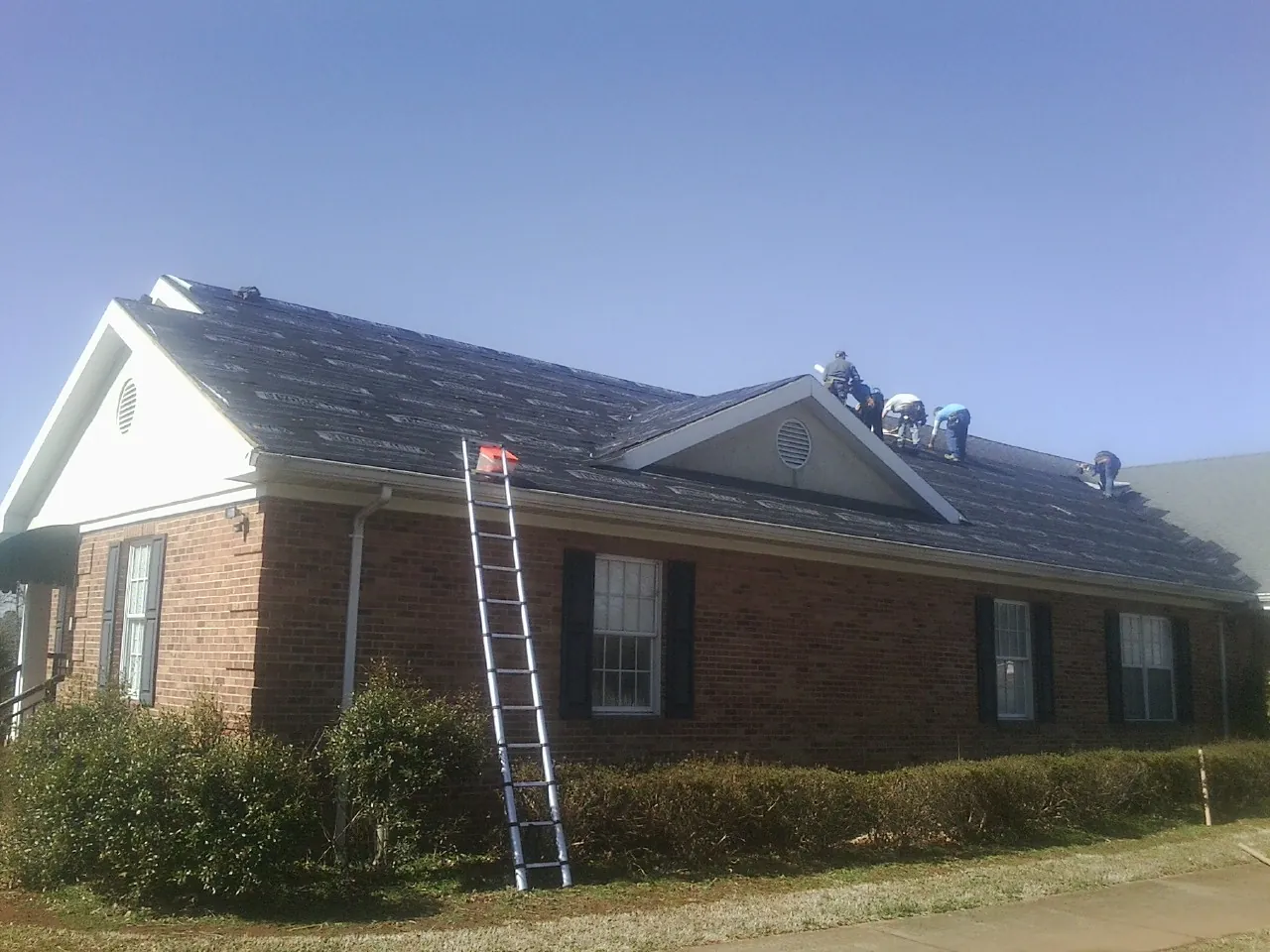 Crew tearing shingles off a brick ranch roof with a ladder set — Emergency Roof Repair work by our crew in Bismarck