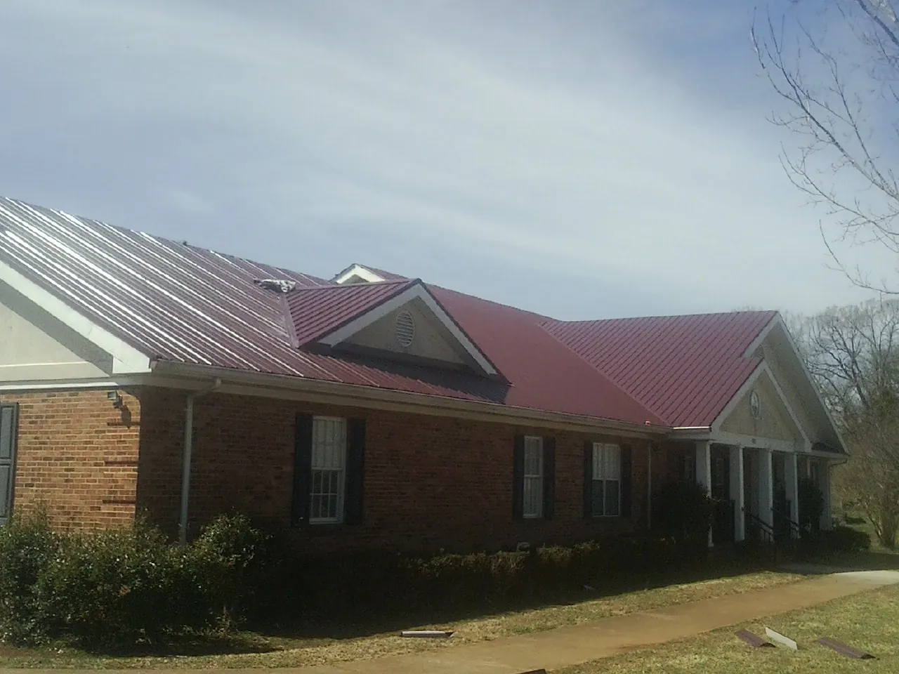 Red metal roof with gabled entries on a long brick building, from a Hail Damage Roof Repair job in Bismarck