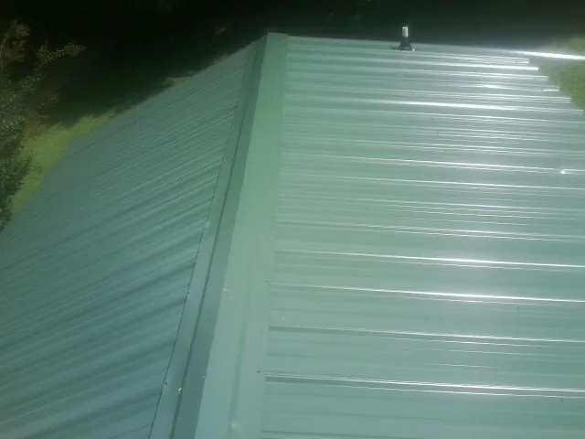 New green metal panels meeting at the ridge of a roof — Flat Roof Repair work by our crew in Bismarck