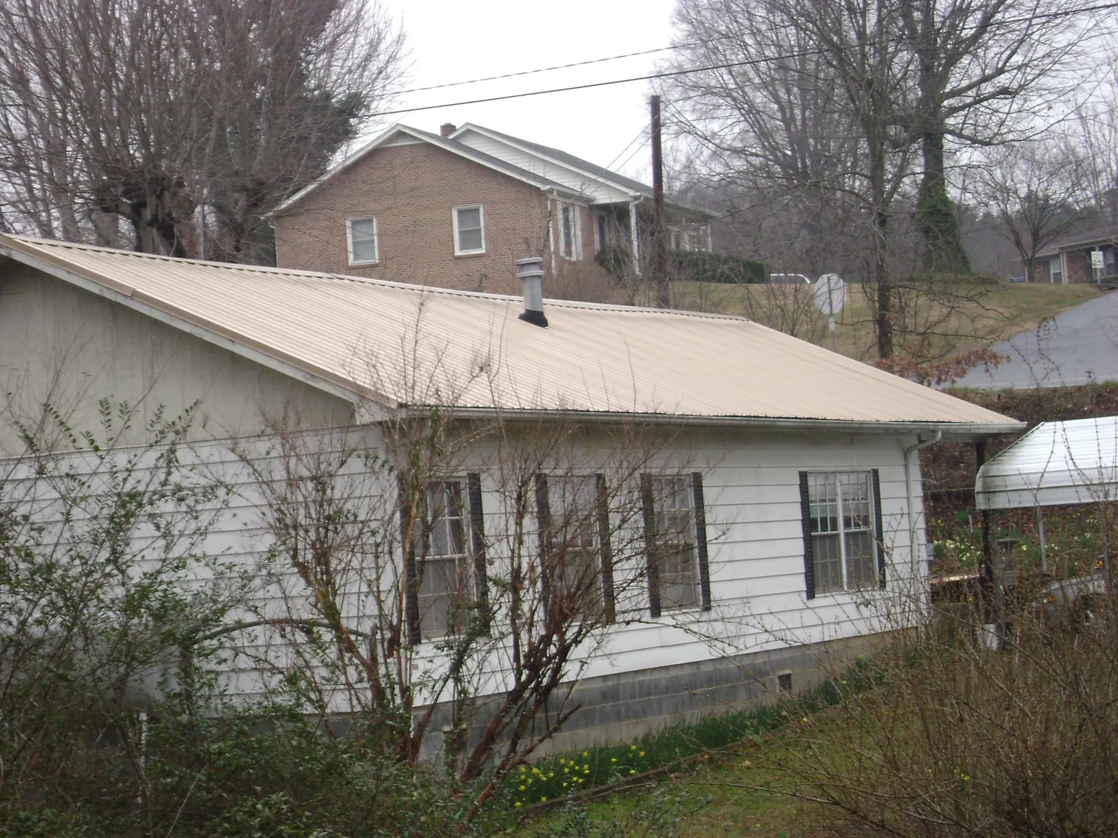 Tan metal roof on a white sided house set into a hillside — Commercial Roofing by Roofing Brothers in Bismarck