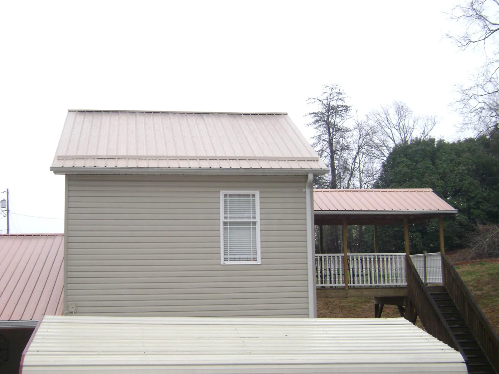 Tan metal roofs on a two story addition and attached porch, from a Roof Replacement job in Bismarck