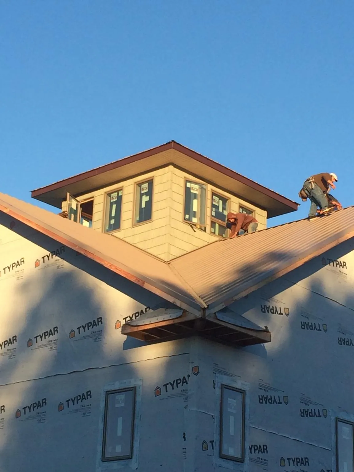 Roofers working around a rooftop cupola on a new metal roof at sunset — Roof Waterproofing in Bismarck by Roofing Brothers